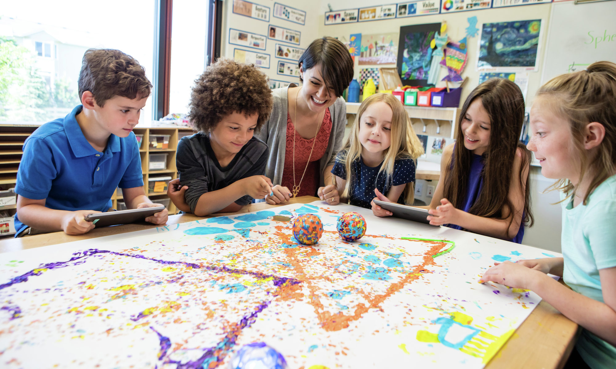 A teacher and children play with a sphero robot in paint